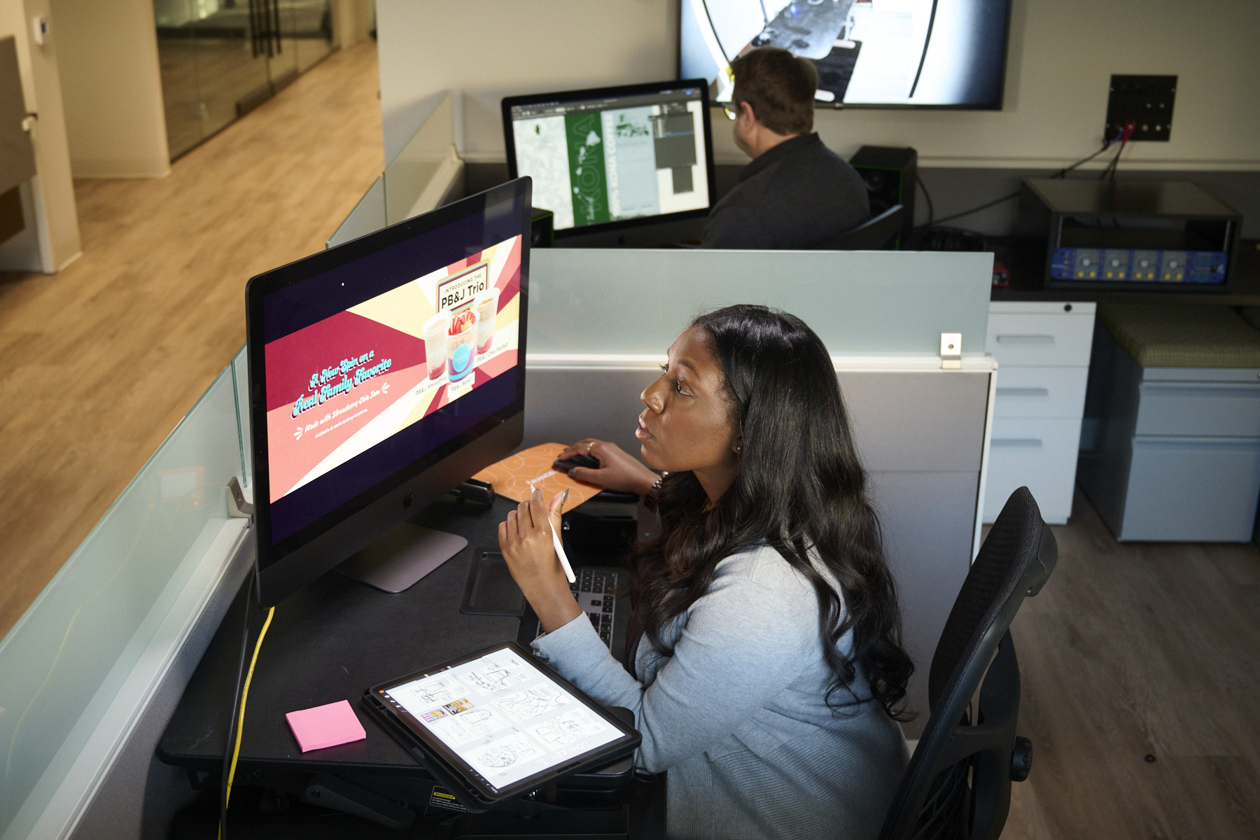 Woman at a desk in a marketing agency looking at a computer screen that shows an image of 3 beverages with the caption "PB&J Trio"