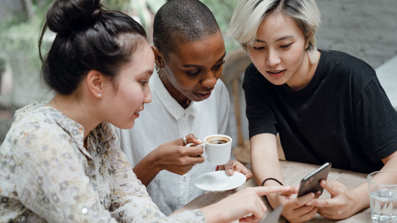 Three young adults looking at a cell phone screen in a cafe while drinking espresso